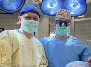 Dr. Connor Berlin, right, made new friends while volunteering his surgical skills in Ukraine, including Dr. Rostislav Malyi, who accepted the gift of a UVA scrub cap.